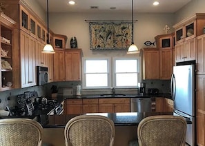 Cocina con armarios de madera, una isla central con sillas, un lavamanos doble y un refrigerador.