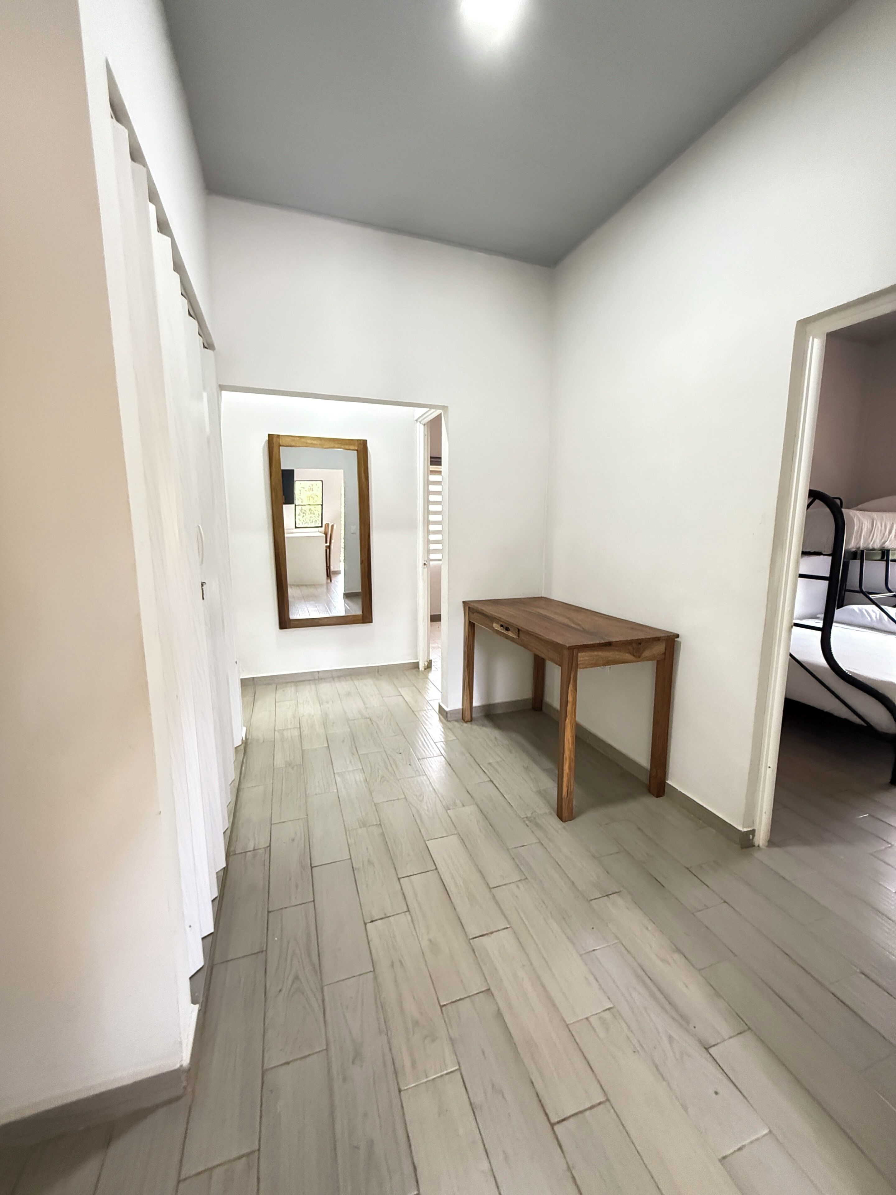 Un pasillo con una mesa de madera, una cama y un espejo.