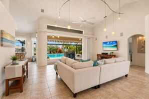 A spacious living area with a large sofa, a dining table, and a TV. There is a pool visible through the glass doors. - Punta Gorda Isles: An Unparalleled Waterfront Luxury Retreat (Punta Gorda)