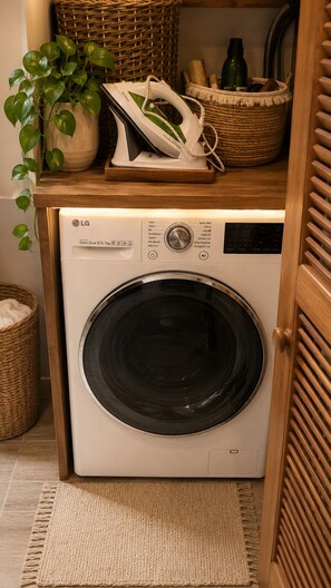A front-loading LG washing machine with a control panel, a wooden shelf above it, and a woven basket to the left. - 1-bedroom apartment, beachfront, in a complex with 3 pools and a garden (anse marcel)