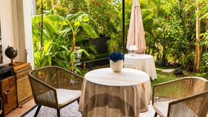 Un patio al aire libre con sillas de mimbre, una mesa redonda con mantel a rayas y un globo terráqueo sobre un aparador.