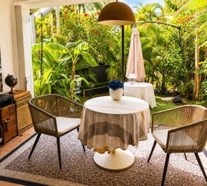 Eine Terrasse im Freien mit Korbstühlen, einem runden Tisch mit gestreifter Tischdecke und einem Globus auf einem Schrank.
