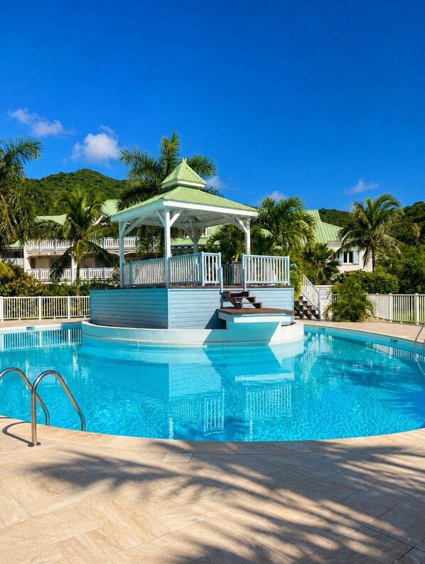 A clear blue pool with a gazebo, palm trees, and a mountainous backdrop. - 1-bedroom apartment, beachfront, in a complex with 3 pools and a garden (anse marcel)