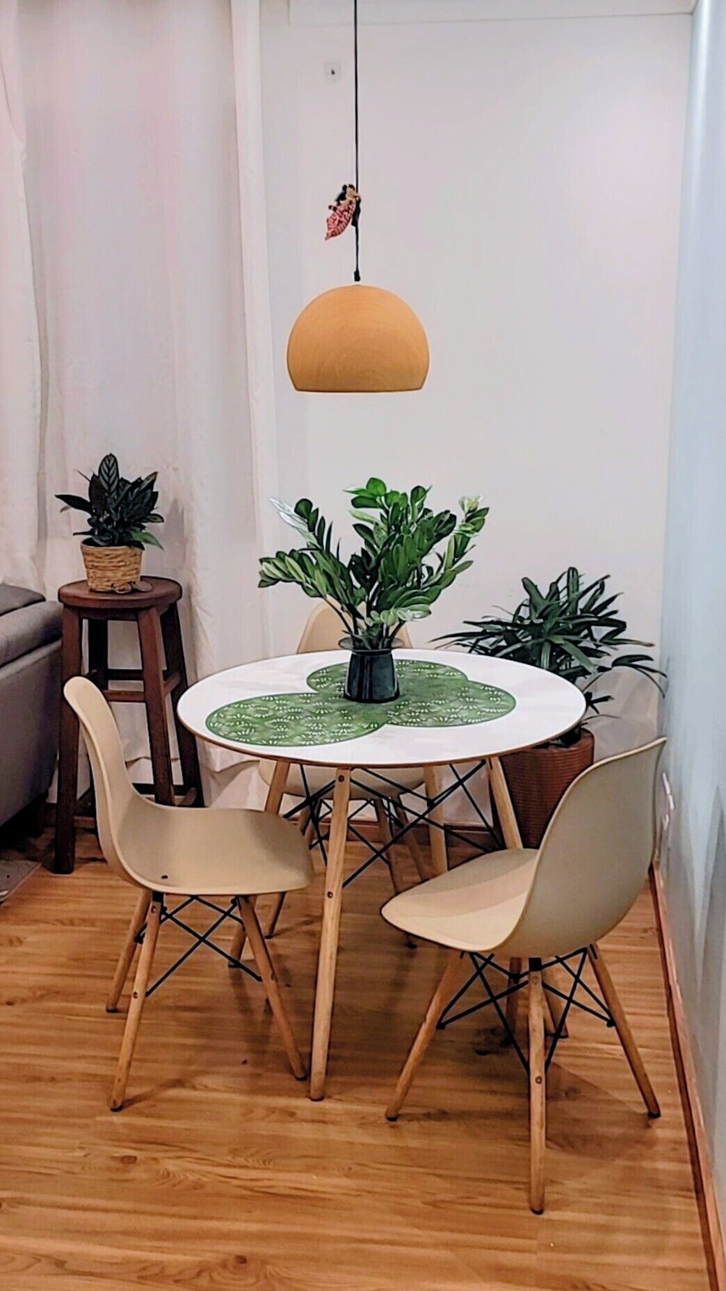 A dining area with a round table, four chairs, a hanging pendant light, and potted plants.