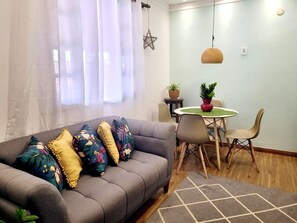 A living room with a grey sofa, floral cushions, a round table with chairs, a hanging pendant light, and a star wall decoration. - RETREAT IN MARICÁ: SUNSET POOL AND DECK. (Maricá)