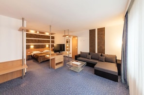 A compact hotel room with a bed, a sofa, a TV, a desk, and a glass coffee table.