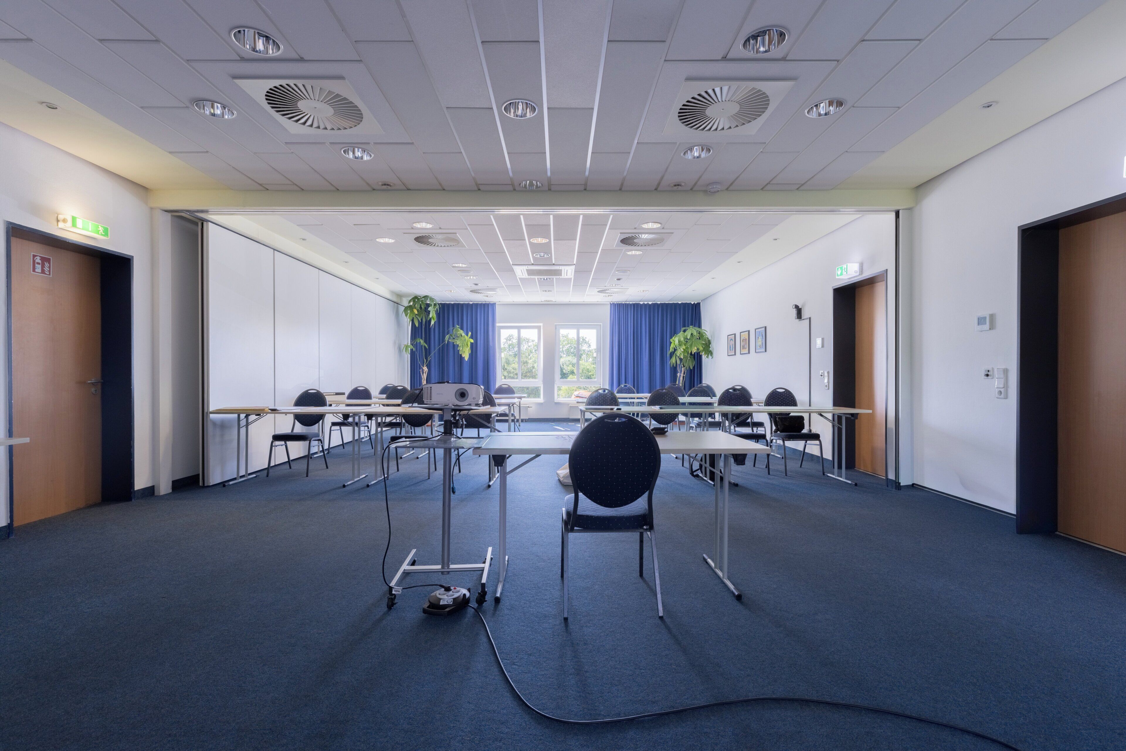 Ein Konferenzraum mit Tischen, Stühlen, einem Projektor und einem Teppichboden.
