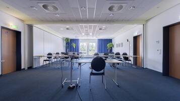 Ein Konferenzraum mit Tischen, Stühlen, einem Projektor und einem Teppichboden.