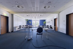 Un salón de conferencias con mesas, sillas, un proyector y piso alfombrado.