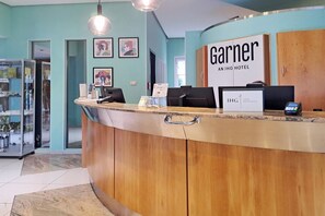 En hotelreception med en trædisk, et skilt med 'Garnier AN IHG HOTEL' og en digital betalingsterminal.