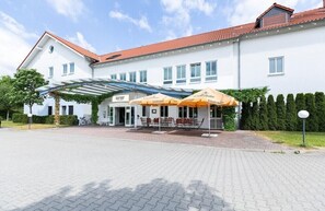 Et hotel med et overdækket udendørs siddeområde, et skilt med 'Garnier' og et rødt tegltag.