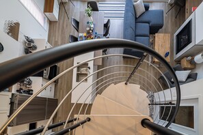 Un interior moderno con una escalera de caracol, un comedor con mesa puesta y una sala de estar con sofá y televisión.