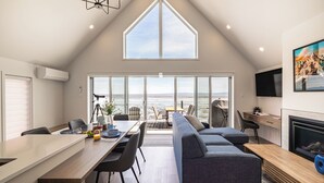Un interior moderno con comedor, sofá, televisión, chimenea y ventanas amplias.