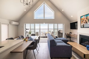 A modern interior with a dining area, sofa, TV, fireplace, and large windows.