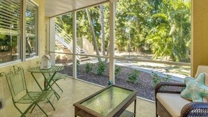 Eine überdachte Terrasse mit Deckenventilator, einem Glastisch und Korbmöbeln.