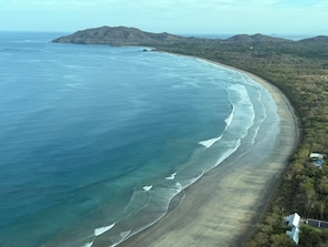 Eine Küstenlandschaft mit einer gewundenen Bucht, Hügeln im Hintergrund und vereinzelter Vegetation.