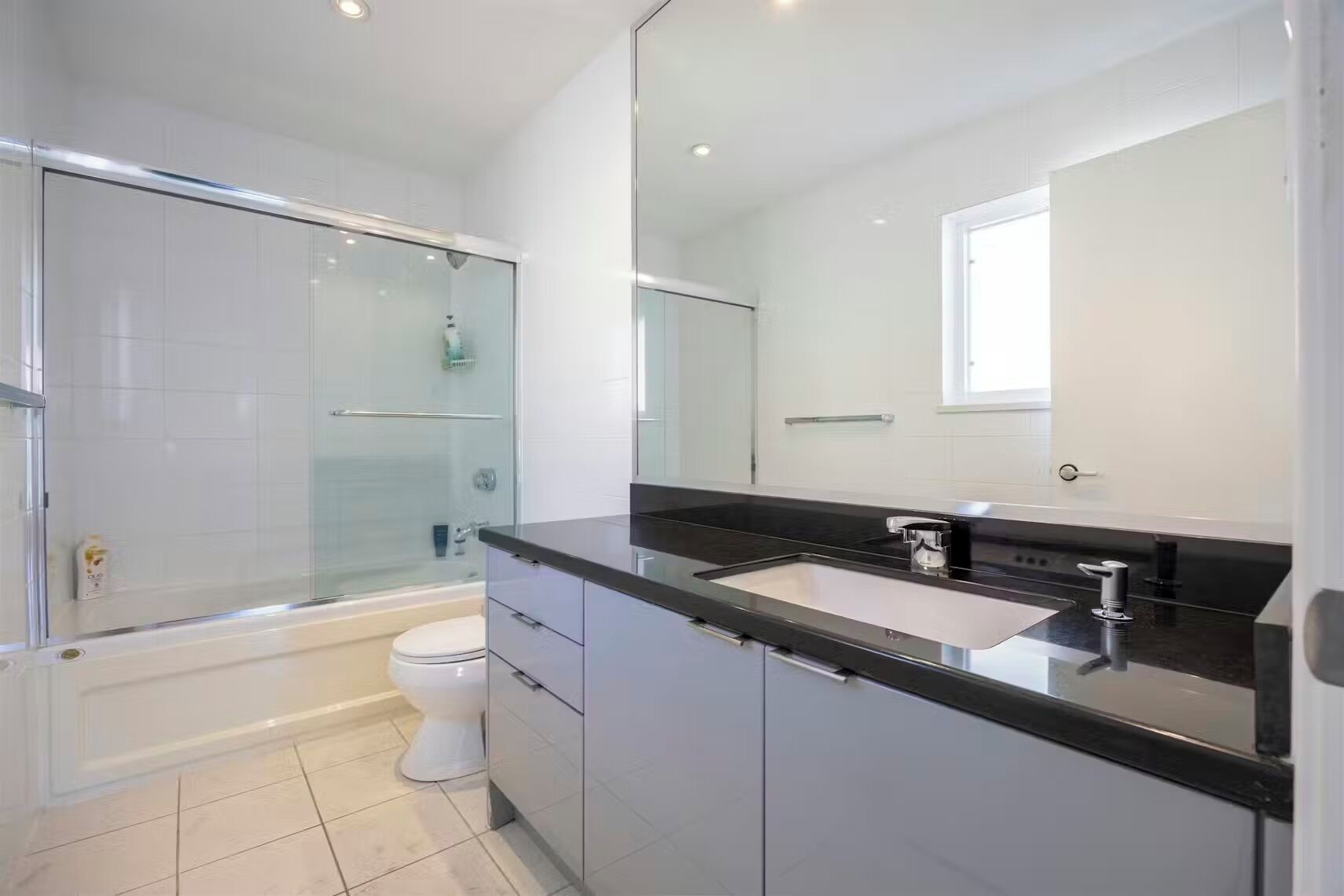 Un baño moderno con cabina de ducha de vidrio, inodoro blanco, encimera negra y un espejo grande.