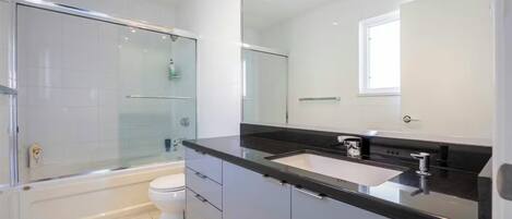 Un baño moderno con cabina de ducha de vidrio, inodoro blanco, encimera negra y un espejo grande.