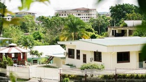 A residential area with a white building, a covered structure, and a large building in the background. - The Barre (Koror)