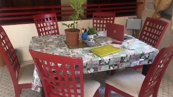 A dining area with a table set for four, surrounded by red chairs, a potted plant, and a laptop on the table.
