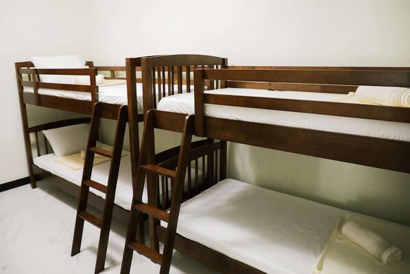 Bunk beds with wooden frames and white bedding, arranged in a room with white walls.
