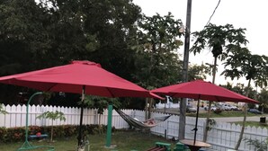 A patio area with two red umbrellas, a hammock, and a barbecue grill. - The Barre (Koror)