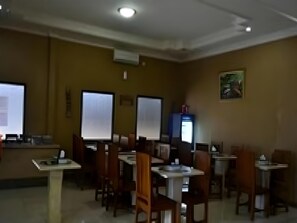 A conference room with tables and chairs, a projector screen, a computer, and a painting on the wall. - Hotel Khalista (Purwakarta)