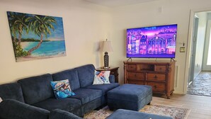 Una sala de estar con un sofá modular, un televisor, un cuadro y un mueble de madera.