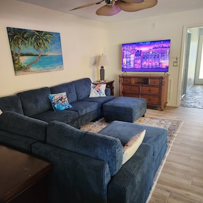 A living room with a sectional sofa, a television, a painting, and a wooden cabinet. - Poolside Paradise (Safety Harbor)