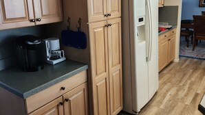 Una cocina con armarios de madera, un refrigerador blanco, una cafetera y una silla azul.