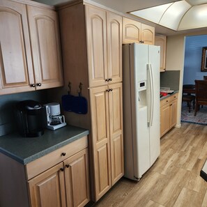A kitchen with wooden cabinets, a white refrigerator, a coffee maker, and a blue chair. - Poolside Paradise (Safety Harbor)