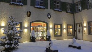 A building with a snow-covered entrance, a lit-up facade, and snow-covered windows. - Jufa Meersburg am Bodensee (Meersburg)