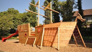A wooden pirate ship play structure with a slide, climbing net, and a ladder. - Jufa Meersburg am Bodensee (Meersburg)