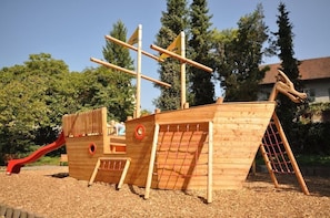 Een houten piratenschip speelconstructie met een glijbaan, klimnet en een ladder.