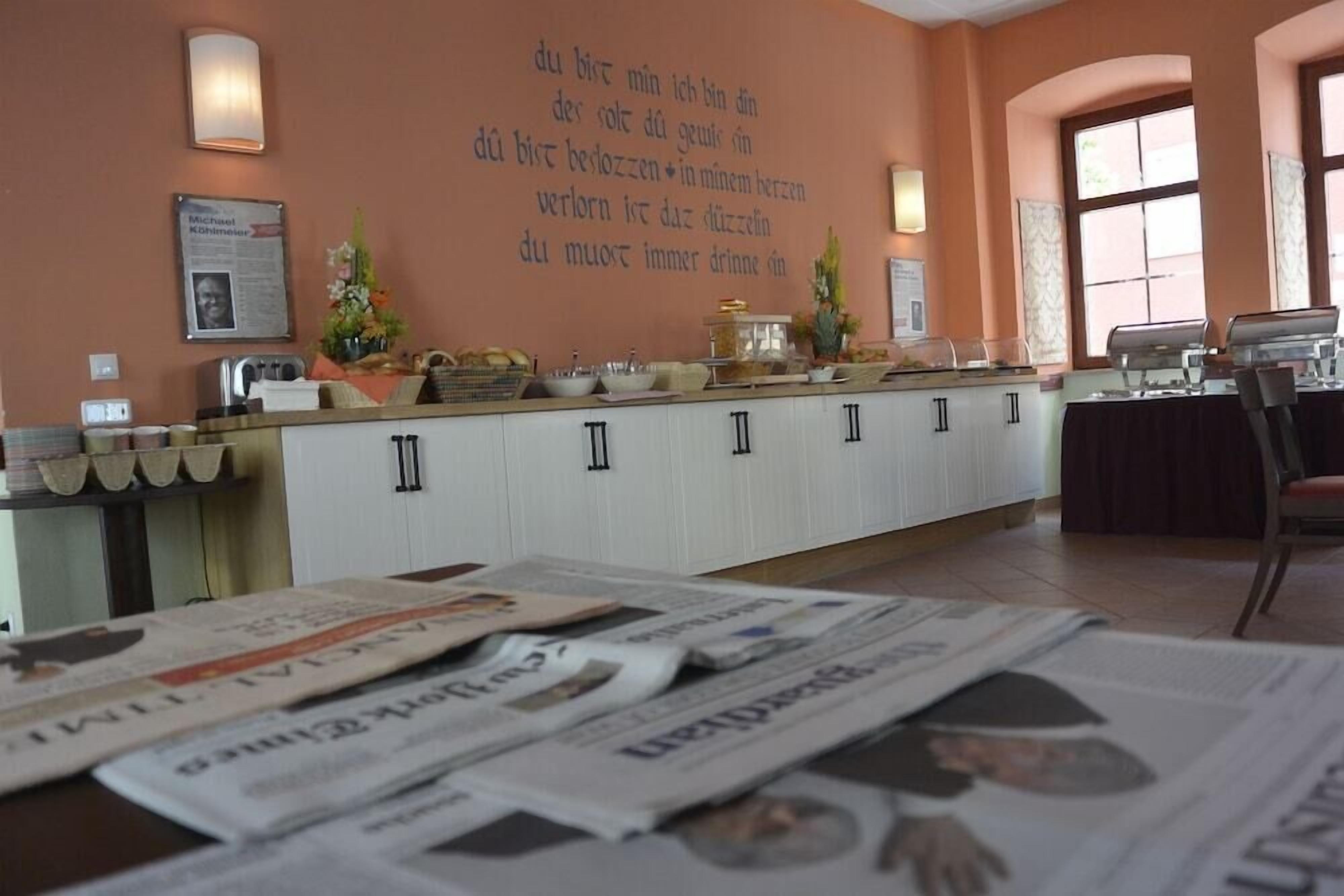 A hotel reception area with a counter, newspapers, a wall with text, and a window.