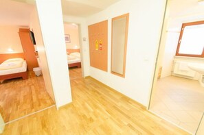 Habitación de hotel con piso de madera, una cama, un espejo y un baño con lavamanos e inodoro.