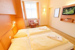 Quarto de hotel com duas camas, uma televisão, uma mesa com cadeira e uma janela com cortinas.