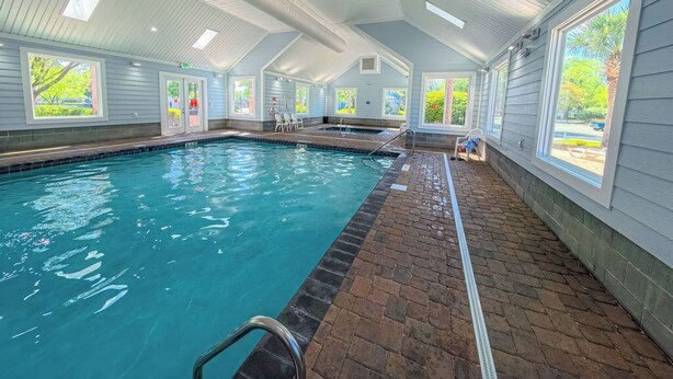 Una piscina interior con suelo de ladrillo, tragaluces y ventanas grandes.
