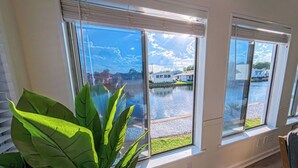 Una habitación con ventanas amplias, una planta en maceta y vistas a un cuerpo de agua y edificios.