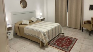 Een slaapkamer met een bed, nachtkastjes, een lamp, een airconditioner, gordijnen, een stoel en een vloerkleed.