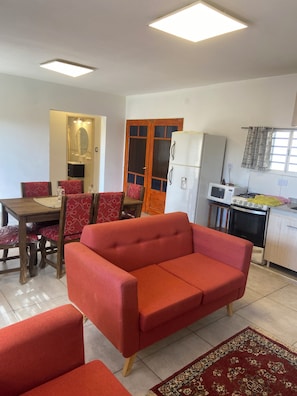 A living room with a red sofa, a dining table with chairs, a kitchen area with a refrigerator, stove, and microwave.