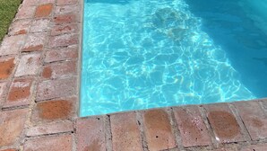 Een rechthoekig zwembad met helderblauw water, omgeven door een bakstenen rand.