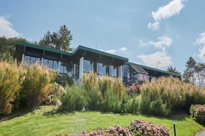 Un edificio moderno con amplias ventanas y techo verde, rodeado de abundante vegetación.