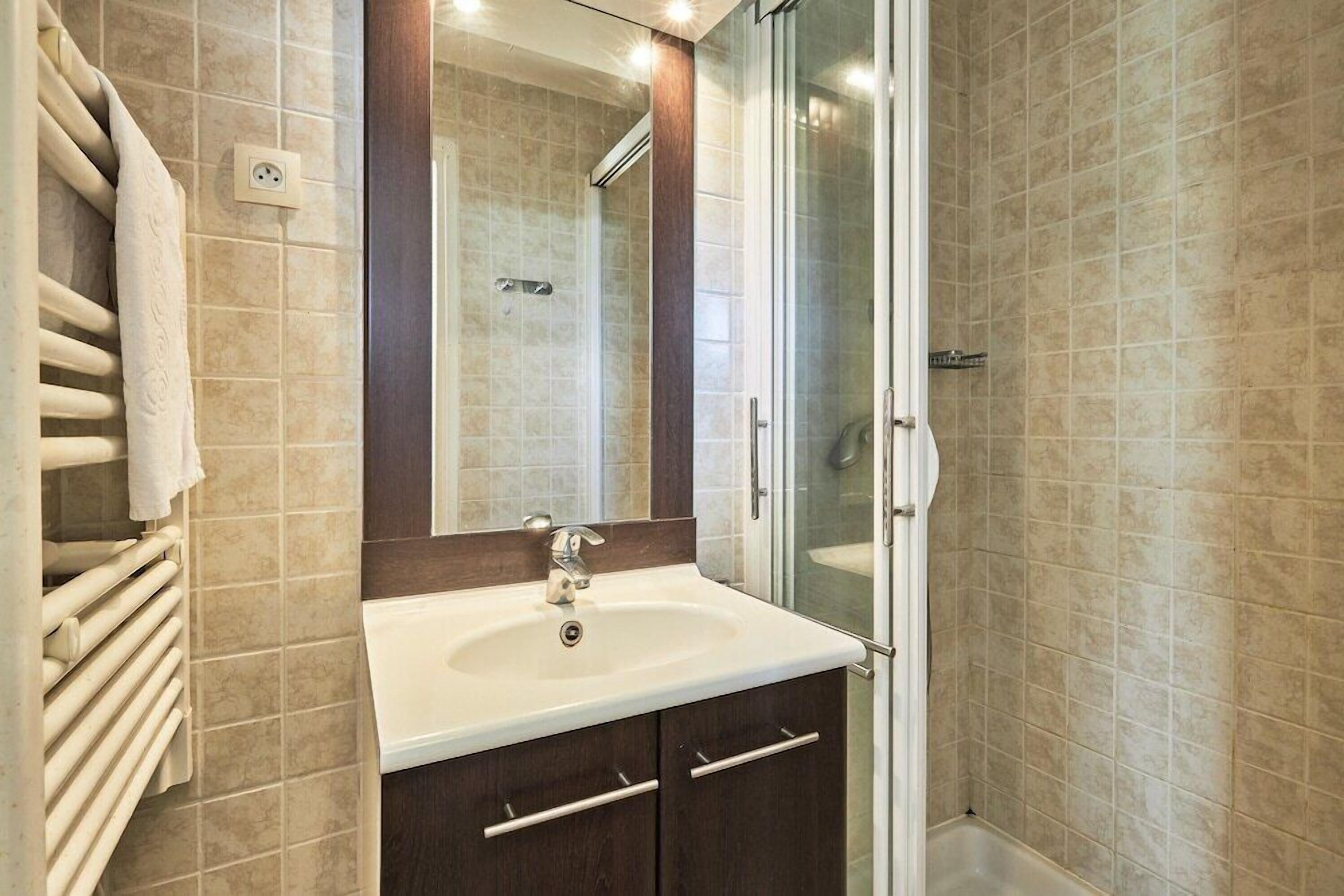 A bathroom with a sink, mirror, and shower.