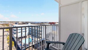 Ein Balkon mit Blick auf ein Schwimmbad und Gebäude, ein Stuhl und ein klarer Himmel.