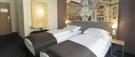 Una habitación de hotel con dos camas, una mesita de noche, una lámpara de pared y un cuadro de un edificio.
