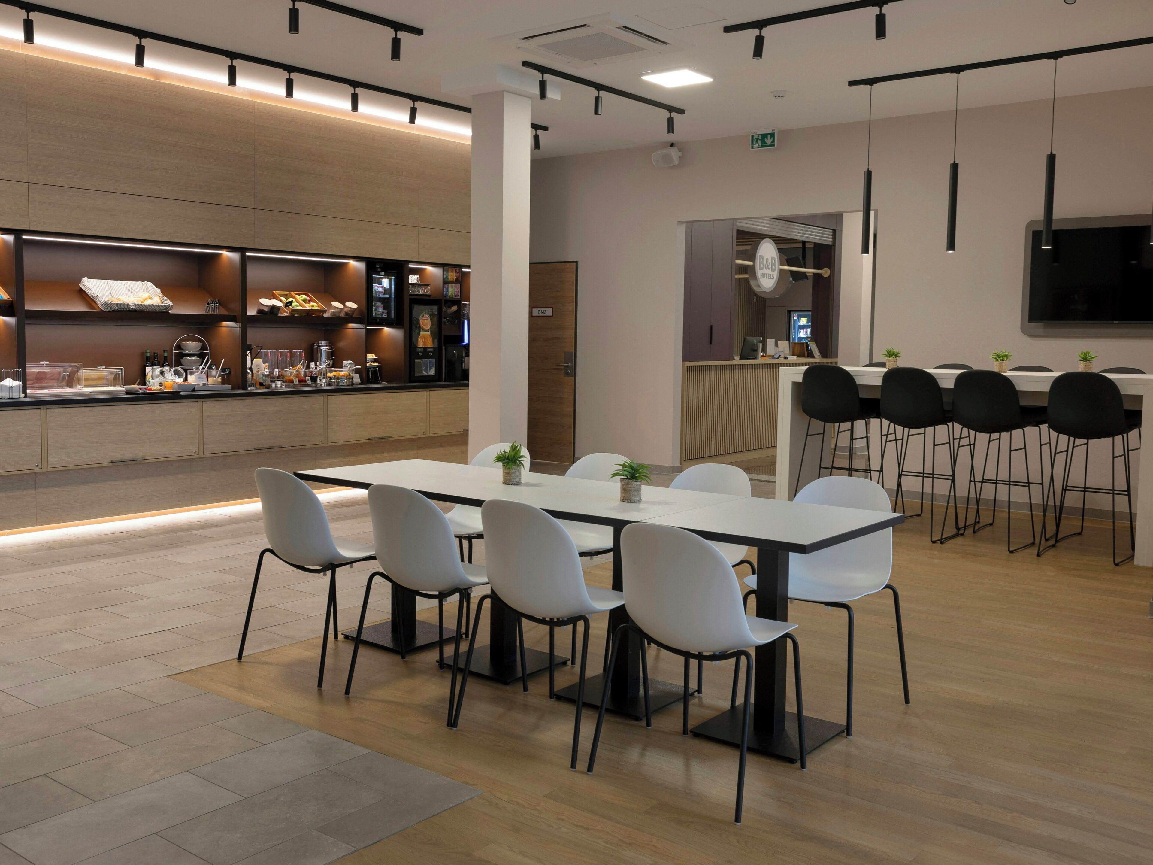Eine moderne Hotelhalle mit einer langen Rezeption, einer Sitzecke mit weißen Stühlen und einer Bar mit Hockern.