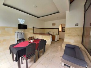 Ein Essbereich mit Tisch, Stühlen, einer Couch und einer Küche im Hintergrund. An der Wand ist ein Fernseher angebracht.