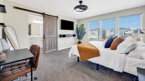A hotel room with a bed, desk, chair, TV, and a sliding door leading to a bathroom. - The Hills in Lorson Ranch (Colorado Springs)