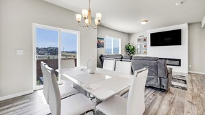 A dining area with a white table and chairs, a chandelier, a flat-screen TV, and a fireplace. - The Hills in Lorson Ranch (Colorado Springs)